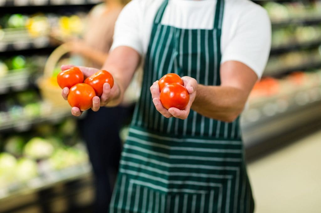 Mid section of worker showing vegetables in supermarket